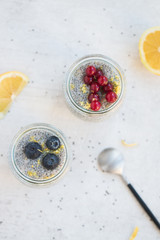 Top view of Jars of chia seed pudding made with chia seeds and almond milk and berries, goose berries, blueberries, lemon zests,  shallow depth of field, copy space and light background. 