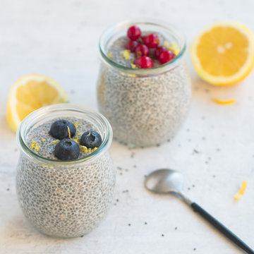 Jars of chia seed pudding made with chia seeds and almond milk and berries, goose berries, blueberries, lemon zests,  shallow depth of field, copy space and light background. 
