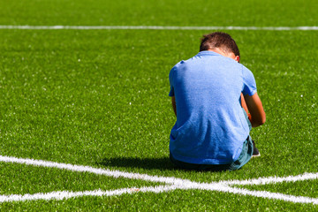 Sad disappointed boy sitting on the grass in stadium