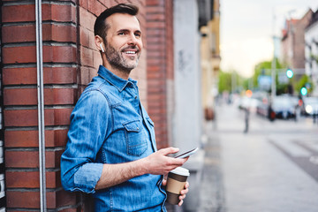 Man chatting on phone through wireless headphones and having coffee