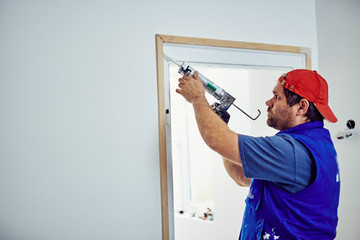 Worker using silicone for walls and door frame inside the house - renovation fixes.