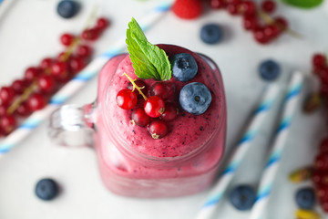 Top view of healthy frozen strawberry and raspberry smoothie in a mason jar glass with a straw, fresh mint and scattered currant, blueberries and blue straws. Overhead, flat lay. 