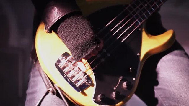 Male musician wearing black leather tight jacket professionally and passionately plays cute bass guitar standing on stage during some concert event.