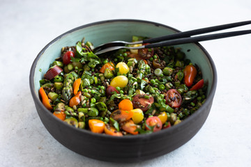 Du Puy lentils, cherry tomatoes, asparagus, sweet peas, scallions, parsley, cilantro, basil salad with vinaigrette in a pottery salad bowl. Side view, light background. 