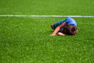 Fototapeta na wymiar Sad alone kid lying on the football field grass outside