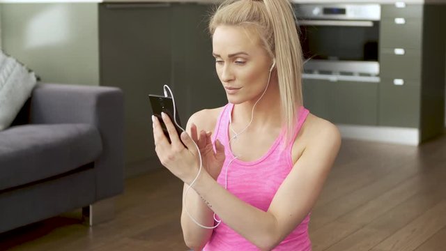 Cute woman sitting on yoga mat and browsing mobile phone for songs