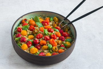 Quinoa, red roasted cherry tomatoes, orange roasted cherry tomatoes and yellow roasted cherry tomatoes, fresh basil salad with olive oil and balsamic in a pottery salad bowl. Side view, natural stone.