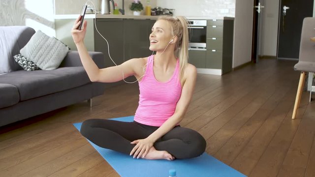 Young attractive sporty woman sitting on yoga mat making selfie with her mobile phone