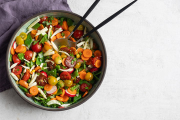 Fennel, flat green beans, cherry tomatoes, radish, carrot, cilantro, parsley, basil, hemp seeds, olive oil, balsamic vinegar salad in pottery dish. Top view, light background