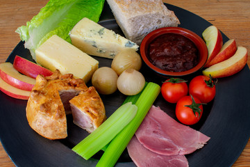 A traditional British meal, Ploughman's Lunch, a cold dish of bread, cheese, meat and onions, on a metal plate.