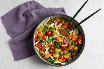 Fennel, flat green beans, cherry tomatoes, radish, carrot, cilantro, parsley, basil, hemp seeds, olive oil, balsamic vinegar salad in pottery dish. Top view, light background