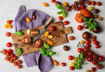 Top view of still life of orange, yellow, heirloom, dark red tomatoes and basil with a wooden chopping board, a rustic knife with a purple napkin. Top view, overhead, good for banner. 