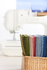 Stack of colorful quilting fabrics in basket on the background of sewing machine