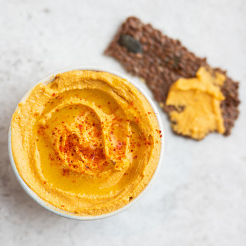Close up of sweet potato or pumpkin or carrot hummus seasoned with paprika and sumac spices, served with seed crackers with flax seeds on a light natural stone table. Top view,.