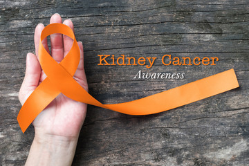 Kidney cancer awareness orange ribbon on human helping hand+ old aged background