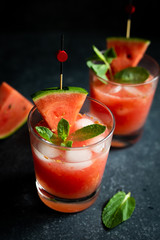 Cold and fresh watermelon juice with ice cubes, fresh mint and a slice of watermelon on a dark natural stone background. Side view, close up. 