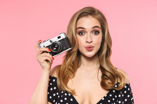 Young pretty woman posing isolated over pink wall background holding camera.