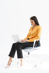 Portrait of cute young businesswoman sitting in chair and using laptop while working in bright...