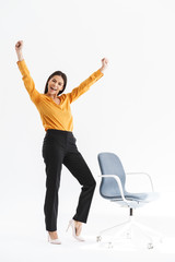 Full length portrait of ecstatic young businesswoman dressed in elegant wear rejoicing and standing by chair