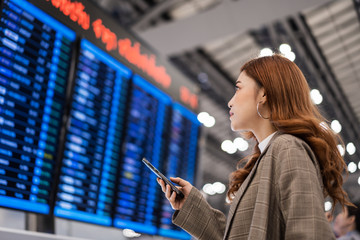 woman using smartphone with flight information board at airport