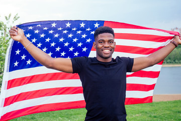 Handsome afro american man with united states flag in hands in summer park near lake evening