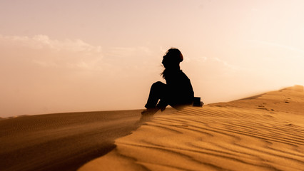 Fototapeta na wymiar silhouette of girl sitting on sand dune at sunset in Sahara Desert, Algeria