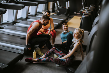 Fototapeta na wymiar Friends in sportswear talking and laughing together while sitting on the floor of a gym after a workout