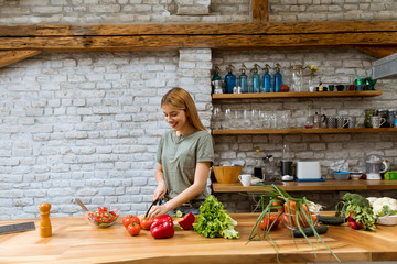 Happy young woman cooking delicious and healthy food in the loft kitchen at home