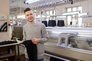 a young man analyzing a knitted piece of cloths near industrial knitted machines with black thread in cones