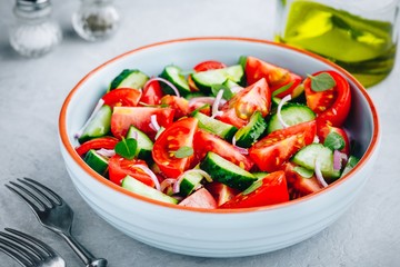 Fresh summer salad bowl with tomatoes, cucumbers, red onions, basil and olive oil dressing.