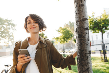 Naklejka premium Young pretty woman walking outdoors in park in beautiful spring day using mobile phone.