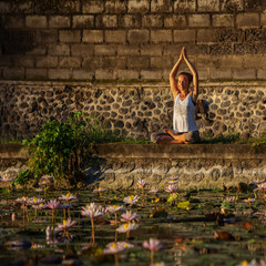 Woman practices yoga on a lake with lotus water lilies