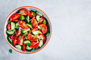 Fresh summer salad bowl with tomatoes, cucumbers, red onions, basil and olive oil dressing.