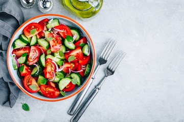Fresh summer salad bowl with tomatoes, cucumbers, red onions, basil and olive oil dressing.