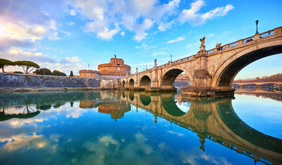 Rome, Italy. Bridge with angels and demons statue in front of Castle of the Holy Angel (Castel Sant Angelo) during evening sunset. Famous touristic landmark. Statues and street lamps medieval.