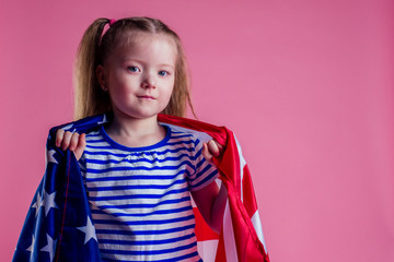 caucasian happy female baby in striped blue and white navy suit holding american flag in hand on a pink background in the studio.English language learning and freedom future profession army navy dream