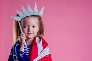 redhead blonde charming female kid celebration independence holding a paper torch and diy crown and american flag on a pink background in the studio.English language learning concept and freedom