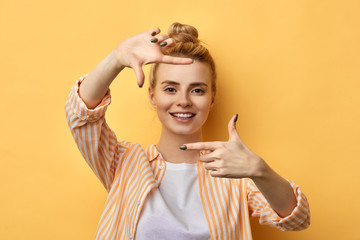 happy blonde woman making frame with fingers isolated on yellow background. close up photo. studio...