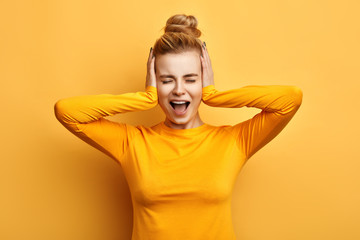 Young woman in stylish yellow sweater screaming in terror with hands on her head, mouth wide open. silence concept. stop talking. I hate you. emotion and feeling