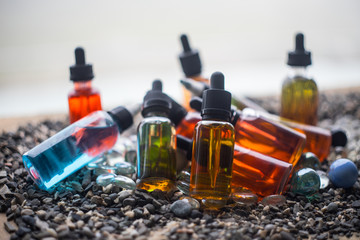 Vape concept. Beautiful colorful vape liquid glass bottles outdoor on stones. Useful as background...