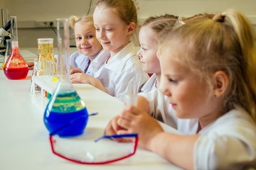group of school girl kids with teacher in school laboratory making experiment observing the chemical reaction with the dye with vinegar and soda volcano wearing white gown uniform glass