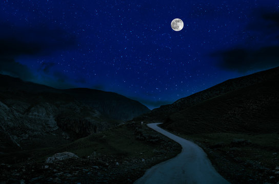 Mountain Road through the forest on a full moon night. Scenic night landscape of country road at night with large moon. Long shutter photo