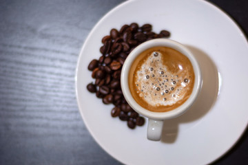 Top view of espresso coffee in a white cup and roasted coffee beans on a saucer. Brown coffee with milk and bubble. Space for text and edit. Close up, selective focus