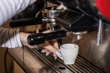 Girl making espresso coffee on a professional machine in the bar. Woman hand holding coffee cup and coffee flows from the machine. Close up, selective focus