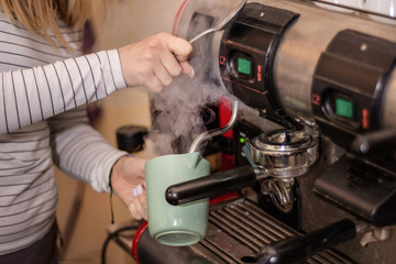 Girl making espresso coffee on a professional machine in the bar. Woman hand holding milk bowl for coffee. The process of making espresso coffee. Close up, selective focus