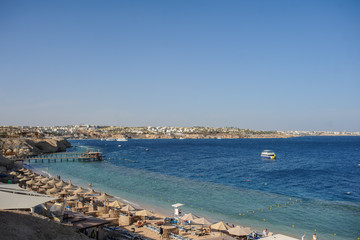 Thatched beach umbrellas and loungers on a beach at an idyllic tropical resort for a summer vacation