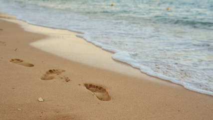 Fototapeta na wymiar Footprints of human feet on the sand near the water on the beach