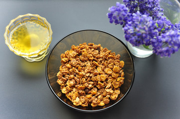 A deep plate bowl with flakes of oatmeal and honey on a dark background with flowers. Healthy breakfast. Proper nutrition.