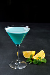 Blue cold cocktail in martini glass with lemon mint dark background