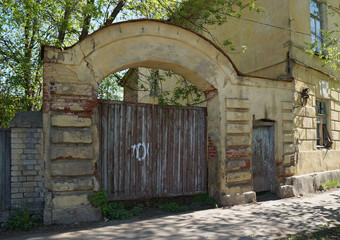 Fototapeta na wymiar Old brick fence with wooden gate. Quiet street with old houses in a small russian town. Sunny day at spring